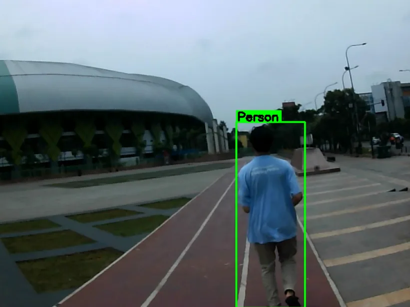 A person detected ahead on the running track, in a green bounding box